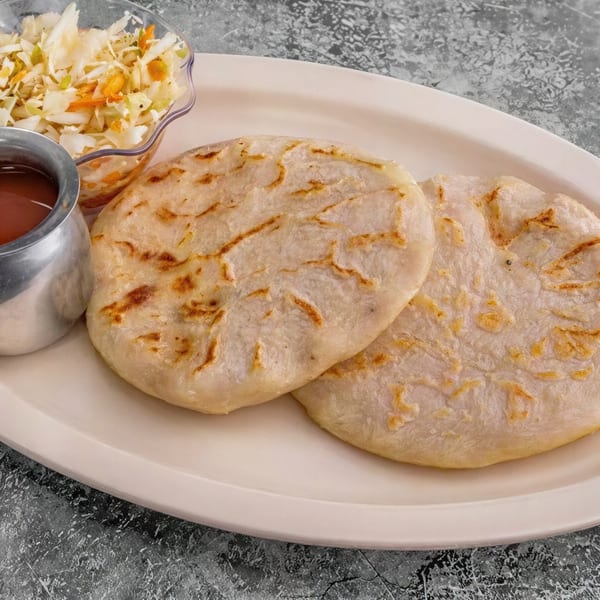 Two pupusas with curtido and red sauce on a white oval plate.