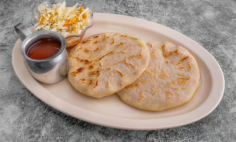 Two pupusas with curtido and red sauce on a white oval plate.