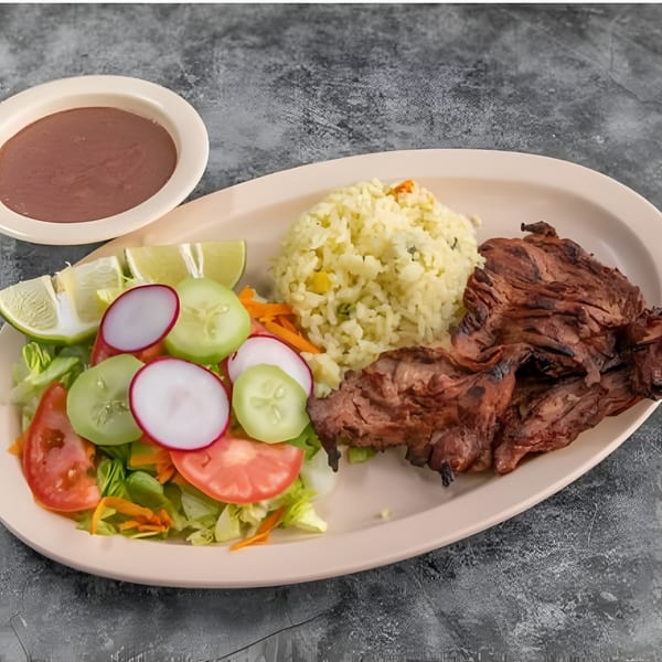 Grilled steak, rice, and a fresh salad with lime wedges and a side of brown sauce.