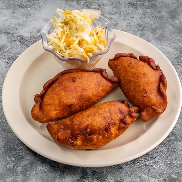 Three golden-brown fried empanadas and a small bowl of coleslaw on a white plate.
