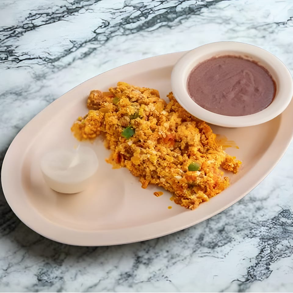 Scrambled eggs with green peppers, a side of refried beans, and sour cream on a marble table.