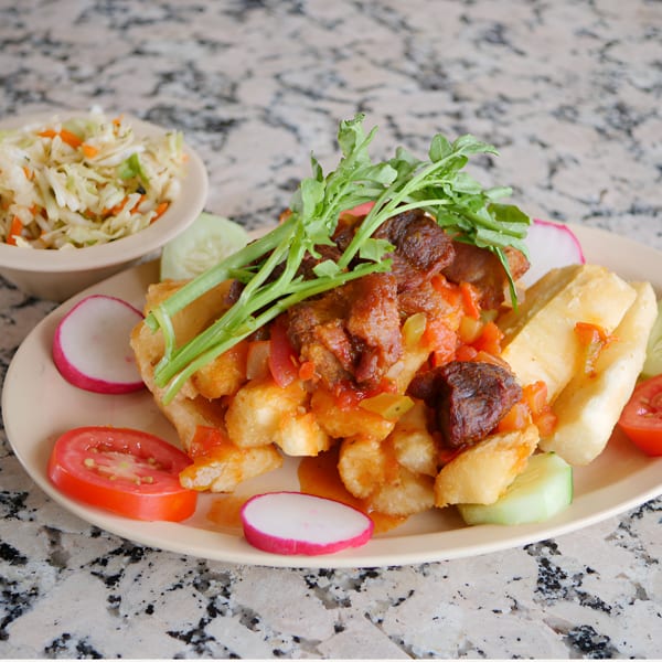 Platter of fried yuca with stewed beef, topped with arugula, served with a side of coleslaw.