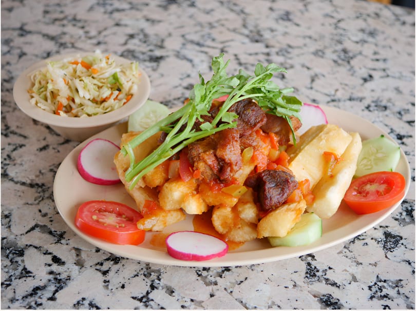 Platter of fried yuca with stewed beef, topped with arugula, served with a side of coleslaw.